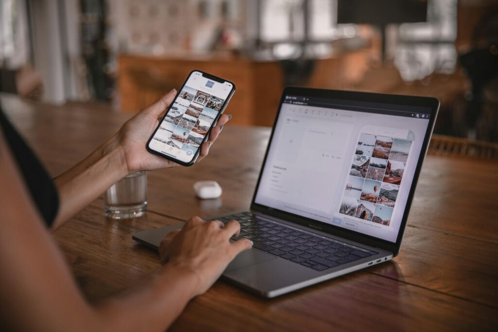 person sitting at wooden table, viewing the same social media platform on their laptop and mobile device